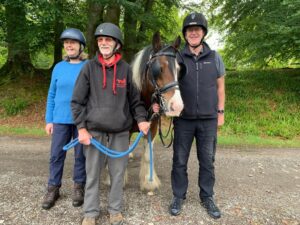 Three volunteers stood with hats on around a pony wearing a driving bridle. 