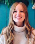 Woman with strawberry blonde hair and wearing a beige turtle neck jumper smiling at the camera